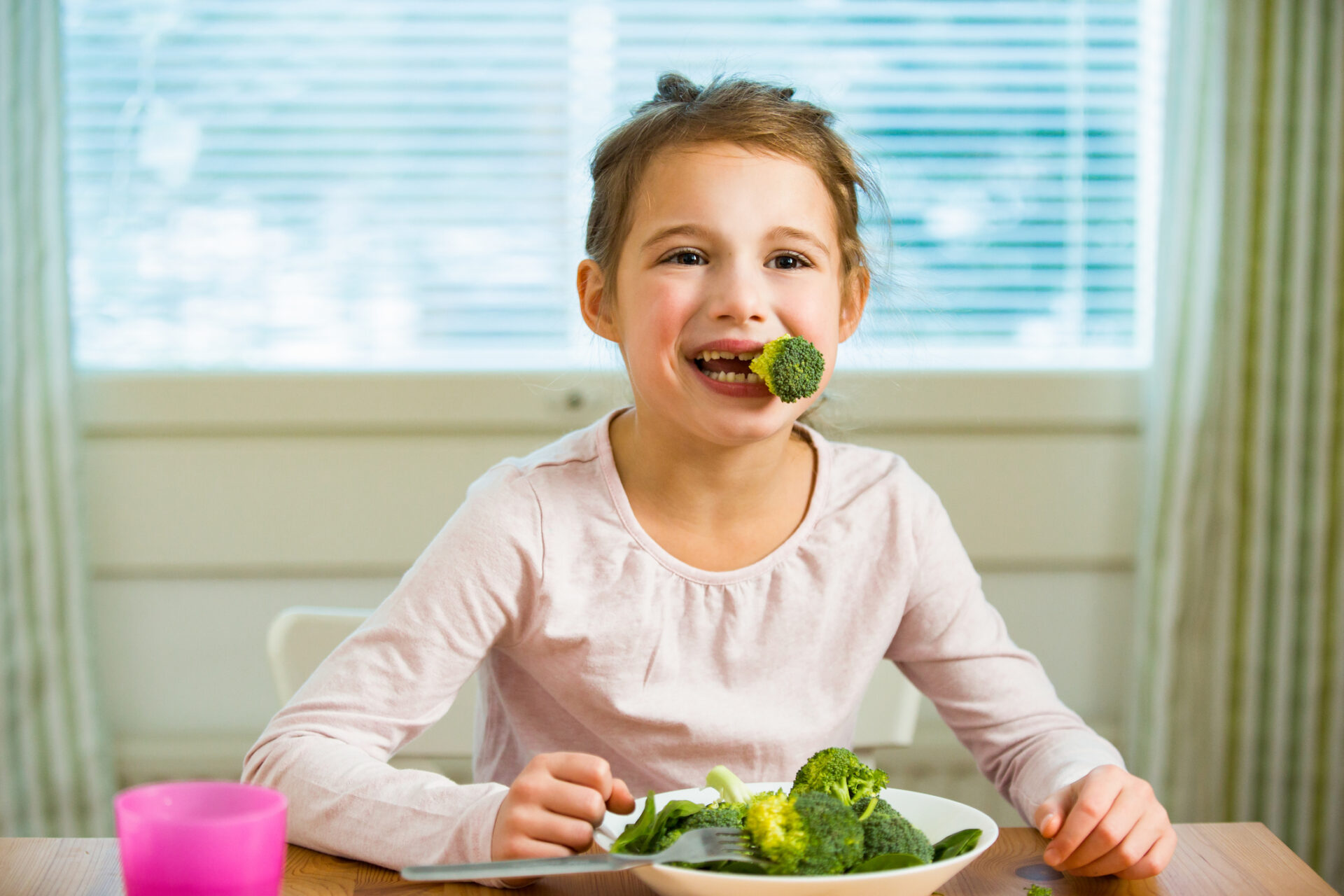 Cute girl eating spinach and broccoli at the table
